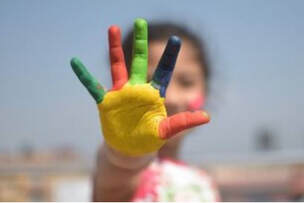 Girl holds out her hand painted in primary colors for Toddler STEAM at our day care, Fort Myers FL..